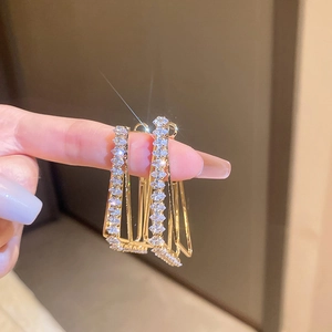 Detailed close-up of golden geometric earrings with three-layer pave-set cubic zirconia stones