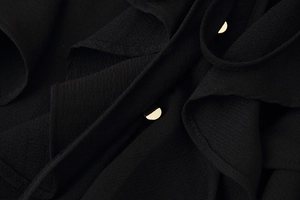 Detailed macro view of black textured fabric with ruffle layers and gold metal buttons
