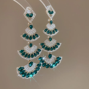 Detail of gold fan-shaped earrings with green emerald gems and diamond tassels