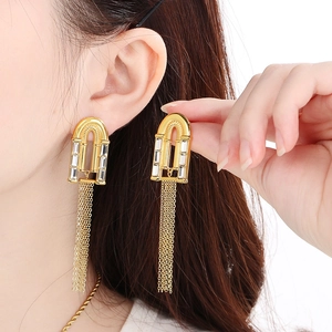 Close-up of gold tassel earrings with white square rhinestones worn by a model