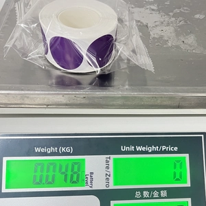 Detail view of purple round label sticker roll on scale showing 0.048kg weight