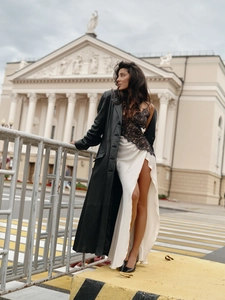 Detail of white satin dress with black lace patchwork and high side slit under leather coat