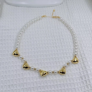 Detail of heart pearl necklace featuring golden heart charms and lobster clasp closure