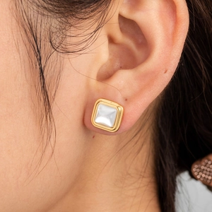 Elegant gold-rimmed square earrings with cream white mother-of-pearl inlay worn on ear