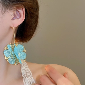 Détails de boucles d'oreilles fleurs bleues et dorées sur mannequin pour un look d'été