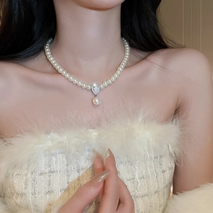 Close-up of pearl necklace with zircon pendant on a model in white feather attire