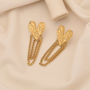 Detail of golden heart hammered metal earrings with layered tassel chains on fabric