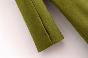 Dettaglio del cappotto di lana verde che mostra la trama del tessuto e le cuciture del polsino