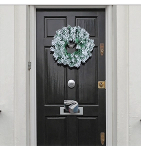 Detail of snowy PVC Christmas wreath hanging on a black front door for festive decor