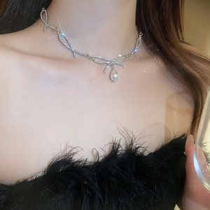 Close-up of a silver bow necklace with sparkling rhinestones and a teardrop pearl pendant
