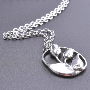 Macro shot of silver tulip pendant with leaf details on an oval stainless steel necklace