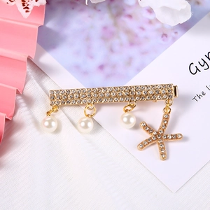 Detail einer goldenen Brosche mit glitzernden Strasssteinen, Perlen und Seestern-Anhänger