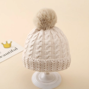 Detail of baby winter knit hat featuring thick cable stitch and soft faux fur pom-pom