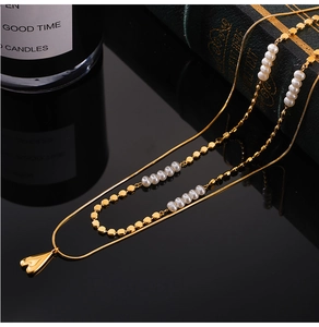Détail du collier doré multi-rangs avec perles blanches et pendentif cœur sur fond noir