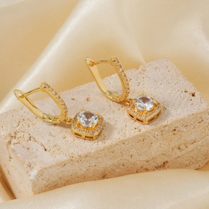 Golden drop earrings with micro-paved cubic zirconia on a beige stone and silk background