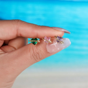 Three dainty gold planet heart earrings with green pink and purple stones on beach