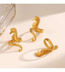 Close-up of golden seahorse rings with intricate texture on a warm beige background