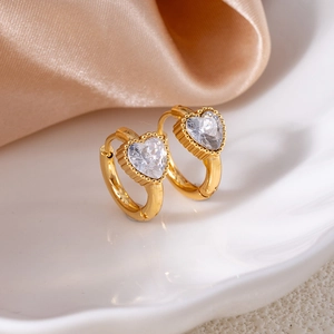 Detail of heart-shaped zircon earrings with gold beaded edges on champagne satin fabric