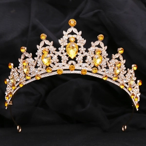 Detailed view of gold leaf crown with yellow gemstones and rhinestones on black velvet