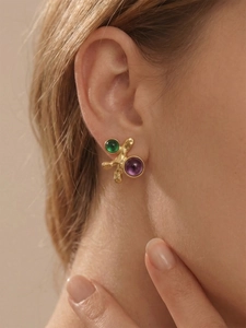 Détail de boucles d'oreilles dorées irrégulières avec pierres vertes et violettes