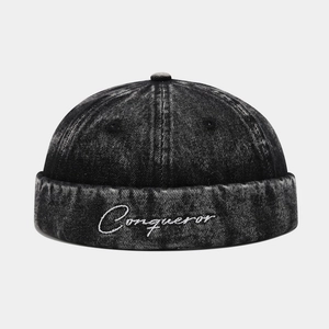 Detailed front view of washed dark grey denim docker hat with white Conqueror embroidery
