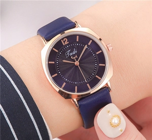 Close-up of square rose gold watch with navy blue leather strap and textured dial