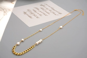 Detail of asymmetrical gold chain necklace with freshwater pearls and heart charm