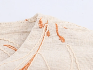 Detail of beige cotton linen fabric featuring intricate orange floral embroidery work