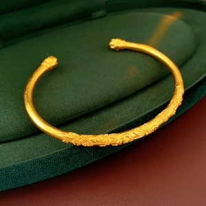 Detailed view of vintage brushed gold bangle with ornate carvings in green velvet box