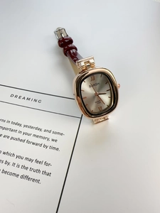 Detail of rose gold cushion-shaped quartz watch with a burgundy leather strap on paper