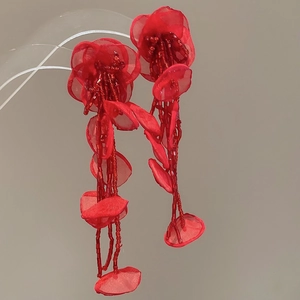 Close-up of handmade red mesh flower earrings with long beaded tassels and leaf details