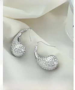 Macro shot of silver teardrop earrings with hammered texture on beige satin fabric
