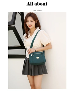 Detail of dark green nylon crossbody bag featuring golden zippers and a metal logo plaque