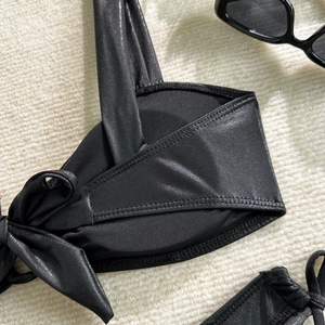 Macro detail of glossy black bikini top featuring a side knot and fine double stitching