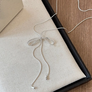 Detail view of silver bow-shaped sliding necklace with snake chain and tassel drops
