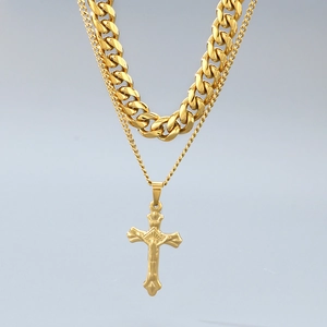 Detail of layered gold stainless steel Cuban chain necklace with a cross pendant