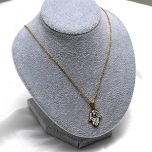 Close-up of golden Hamsa Hand necklace with Evil Eye and zircon on jewelry bust