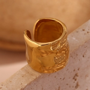 Dettaglio macro di un anello largo aperto placcato oro con texture a onde e finitura lucida