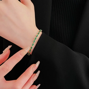 Detail of a green gemstone bracelet with gold chain worn by a model on black fabric