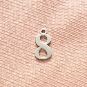 Close-up of polished silver number 8 pendant on a soft pink textured fabric background