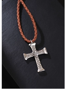 Macro shot of a silver cross pendant with hammered texture and heart motif on brown leather