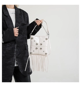 White square shoulder bag with silver round rivets and long tassel details worn by model