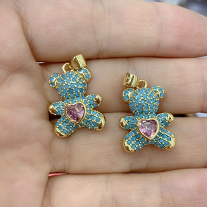 Handheld view of gold bear pendants with blue turquoise inlay and pink heart stone