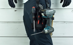 Detail of a black nylon tool leg bag worn on the thigh holding a heavy-duty electric drill