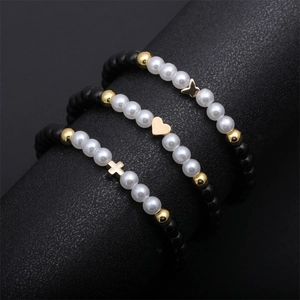 Three-piece beaded bracelet set featuring heart, cross and butterfly charms on black stand