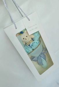 Close-up of blue soap roses with a cute teddy bear in a white gift bag with window