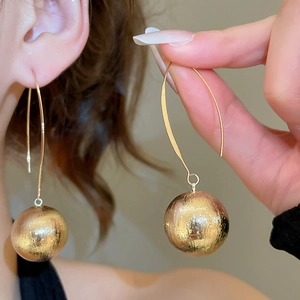 Detail of golden drop hook earrings with brushed texture sphere pendant on model
