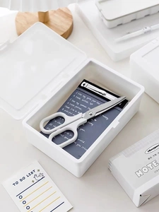 Flat lay of a white minimalist plastic storage box with scissors and stationery items