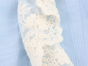 Detailed macro view showing delicate white floral lace embroidery on light blue fabric