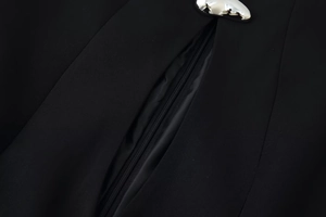 Detailed close-up of a black dress featuring a silver metal fastener and zipper seam